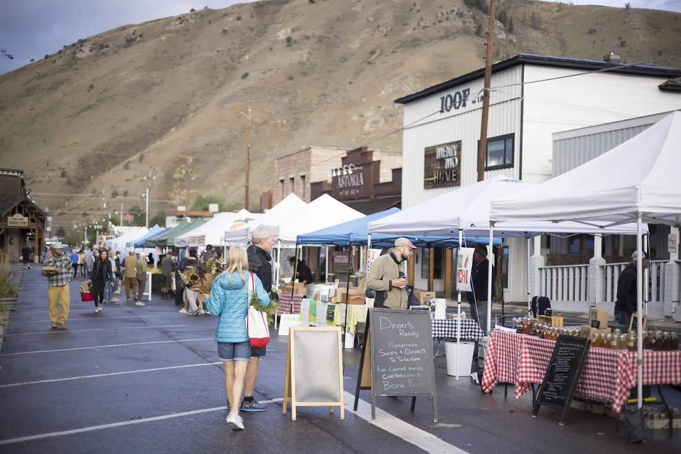 A summer street market in Jackson, with canopies and shoppers below a green hillside.