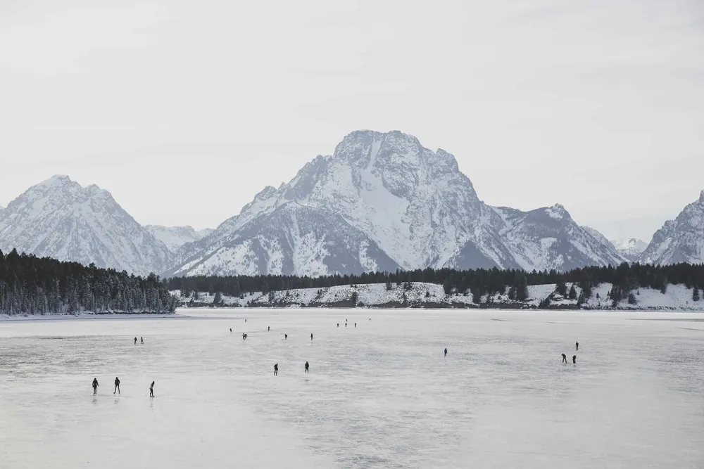 Mount Moran above a frozen lake, with a few skaters out on the ice.